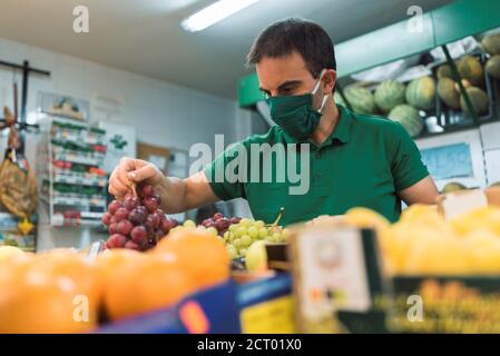 Un uomo che indossa una maschera raccogliendo un mazzo di uve nere. Concetto di cibo Foto Stock