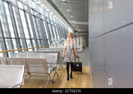 Felice passeggero femmina con i bagagli a piedi nella sala vuota di terminal dell'aeroporto Foto Stock