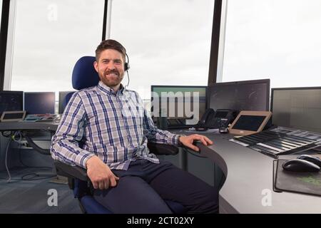 Uomo con la cuffia seduto sulla sedia nell'ufficio del dispatcher e sorridendo Foto Stock