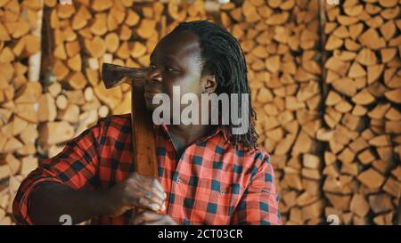 Uomo africano con l'ascia in piedi davanti a pila di legname tagliato per l'inverno. Foto di alta qualità Foto Stock