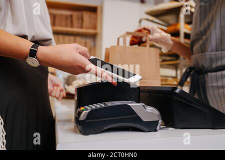 Donna in un negozio di panetteria che fa un acquisto, pagando con il suo telefono Foto Stock