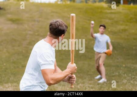 vista posteriore del padre che tiene la mazza di softball mentre gioca il baseball con figlio adolescente Foto Stock