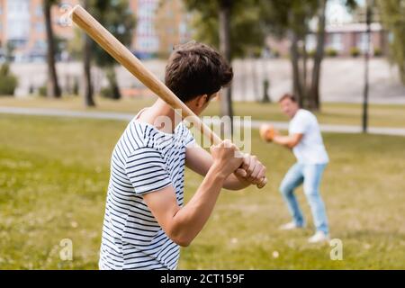 vista posteriore del figlio adolescente con softball bat che gioca a baseball con il padre nel parco Foto Stock