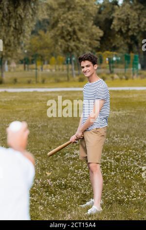 fuoco selettivo del figlio adolescente gioioso che tiene il bat di softball vicino padre nel parco Foto Stock