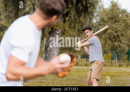 fuoco selettivo del ragazzo teenager che tiene il bat di softball e che gioca baseball con l'uomo nel parco Foto Stock