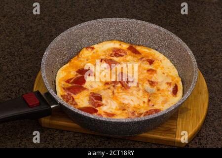 Omelette con pomodori in una padella sul taglio pensione sul tavolo bachelor cibo Foto Stock