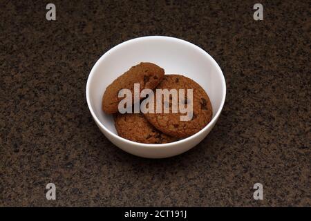 Biscotti di farinata d'avena con pezzi di cioccolato in una ciotola bianca sul tavolo marrone Foto Stock