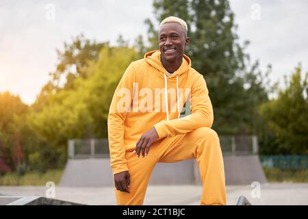 afroamericano sorridente nero uomo giallo felpa con cappuccio fuori emozionale felice afro Modello Guy Walking skate Park estate giorno spazio libero positivo emozioni Foto Stock