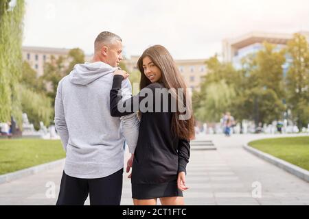 Coppia in amore camminare all'aperto parco fontana caucasico uomo asiatico Donna cammina all'esterno vestiti da sport vista posteriore Foto Stock
