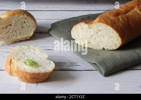 Baguette di pane fresco e morbido alla francese su tovagliolo e sfondo di legno. Diversi pezzi tagliati sono stesi l'uno accanto all'altro. Foto Stock