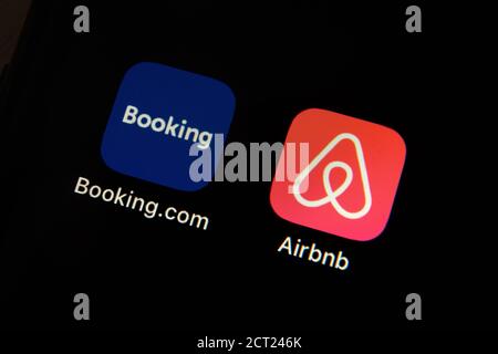 Mani che tengono iPhone 11 con Airbnb e booking.com icone di servizio. Crisi del settore alberghiero e dei viaggi a causa della ristrutturazione pandemica di Covid o Coronavirus Foto Stock