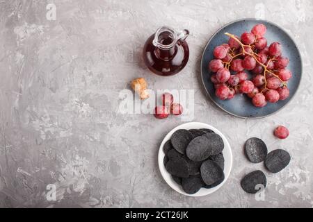 Patatine nere con carbone, aceto balsamico in vetro, uva rossa su un piatto di ceramica blu su fondo grigio di cemento. Vista dall'alto, disposizione piatta, COP Foto Stock