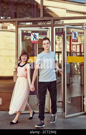 La giovane coppia caucasica sta uscendo dalla stazione metropolitana mano in mano mentre l'uomo tiene una porta di vetro. Foto Stock