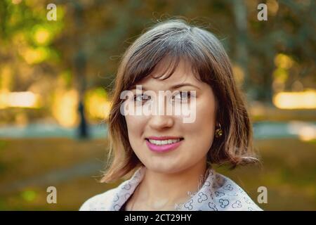 Ritratto di sorridente giovane bella donna caucasica di 25 anni durante la passeggiata nel parco pubblico di giorno. Foto Stock