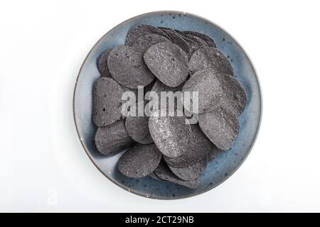 Patatine nere con carbone su una piastra di ceramica blu isolata su sfondo bianco. Vista dall'alto, disposizione piatta, primo piano. Foto Stock