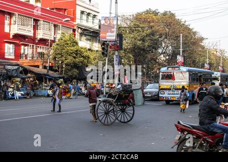 Kolkata, India - 1 febbraio 2020: Un uomo non identificato con il suo risciò attraversa la strada da una fermata del traffico con autobus e auto a un semaforo rosso Foto Stock