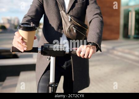 Mani di un elegante uomo d'affari che tiene un bicchiere di caffè e cavalcare su scooter Foto Stock