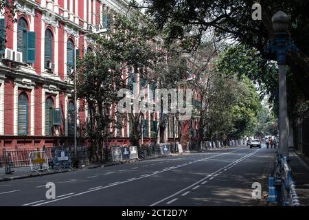 Kolkata, India - 1 febbraio 2020: Tre persone non identificate camminano sulla strada con due auto di passaggio accanto ad una facciata casa rossa il 1 febbraio 2020 Foto Stock