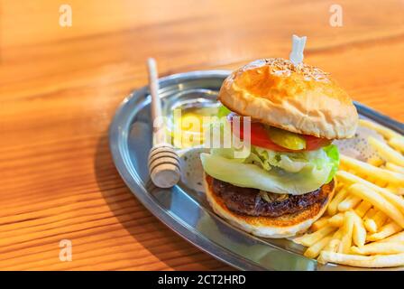 Delizioso hamburger con succulente patatine e lattuga in ciambelle di semi di sesamo con patate fritte e un cucchiaino per la salsa al miele. Foto Stock