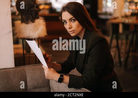 Donna professionale di affari che indossa abbigliamento di moda in ristorante sta scrivendo in documenti cartacei. Foto Stock