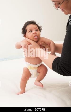 Sviluppo infantile neonato bambina di 6 settimane di età tenuta in posizione verticale da passo riflesso madre Foto Stock