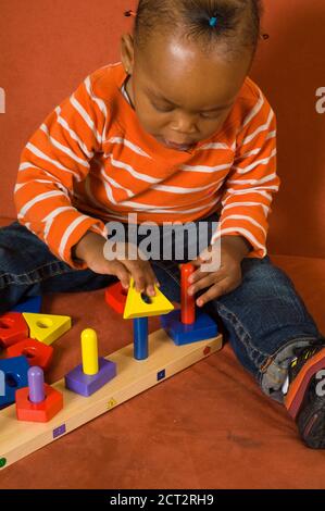 bambina di 20 mesi che gioca con un giocattolo colorato smistatore di forma geometrica in legno verticale Foto Stock