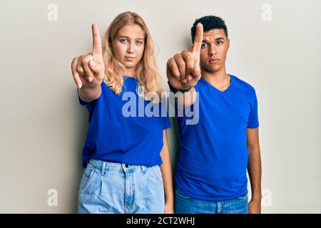 Giovane coppia interracial che indossa abiti casual puntando con il dito verso l'alto e l'espressione arrabbiata, non mostrando alcun gesto Foto Stock