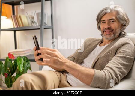 Felice uomo maturo bearded che ti guarda con sorriso mentre seduta in poltrona Foto Stock