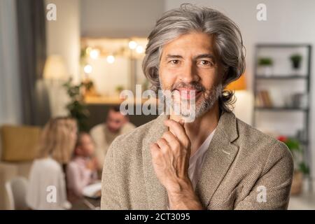 Felice uomo maturo bearded in casualwear che tocca il mento mentre si guarda a te Foto Stock