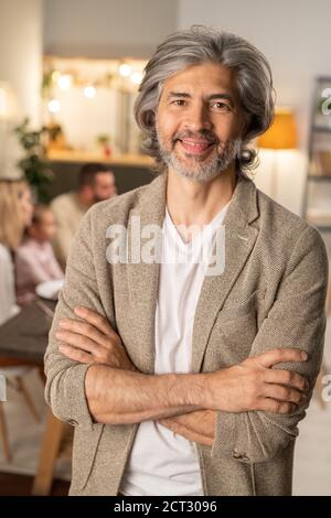 Uomo dal barbuto allegro e dai capelli grigi in casualwear che attraversa le braccia torace Foto Stock