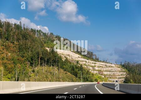 Vista panoramica dell'ingresso del tunnel nelle montagne della Croazia. Bellissimo paesaggio con montagna e foresta, autostrada con auto rossa Foto Stock