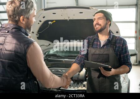 Felice giovane tecnico di servizio auto scuotendo mano di maschio cliente dopo la riparazione Foto Stock