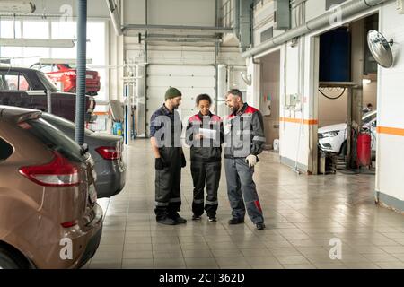 Tre lavoratori interculturali del centro di manutenzione auto che hanno discusso Foto Stock