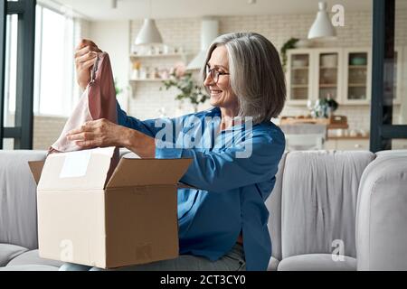 Felice metà invecchiata donna apertura pacco disimballaggio postale consegna scatola a casa. Foto Stock