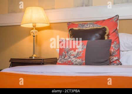 Interni con camera da letto con cuscini rossi, letto, comodino in legno e lampada in un hotel boutique di lusso, Buenos Aires, Argentina, Sud America Foto Stock