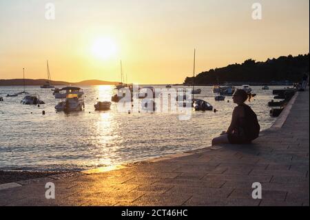 Foto di un turista seduto guardando il tramonto nel porto della città di Hvar, isola di Hvar, Dalmazia, Croazia Foto Stock