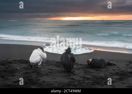 I turisti scattano una foto degli iceberg all'alba sulla spiaggia di Jokulsarlon, una spiaggia di sabbia vulcanica nera nel sud-est dell'Islanda, in Europa Foto Stock