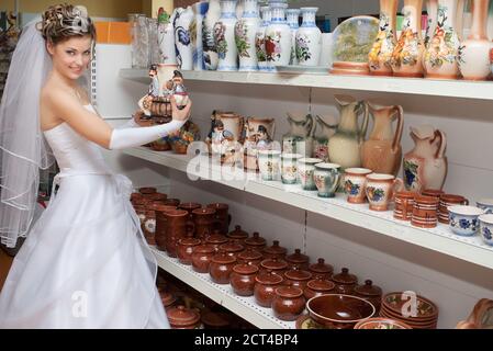 Sposa sorridente che prende un vaso di fiori da scaffale in ceramica un negozio Foto Stock