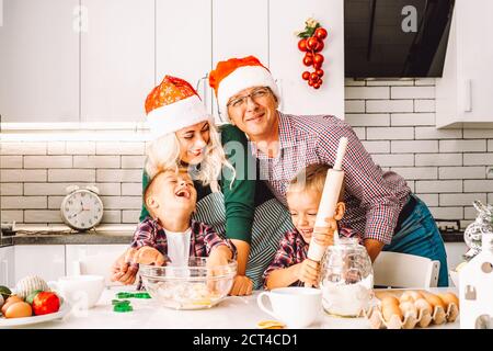 Famiglia di due ragazzi gemelli e genitori di età che preparano i biscotti Per la vigilia di Natale in cucina leggera indossando cappelli Santa Foto Stock