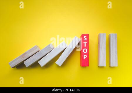 Blocchi di legno con Stop Text arresto che cade Dominos su giallo. Concetto di pensiero creativo e logico Foto Stock