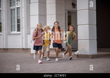 Scolari che corrono felicemente mentre lasciano la scuola dopo le lezioni Foto Stock