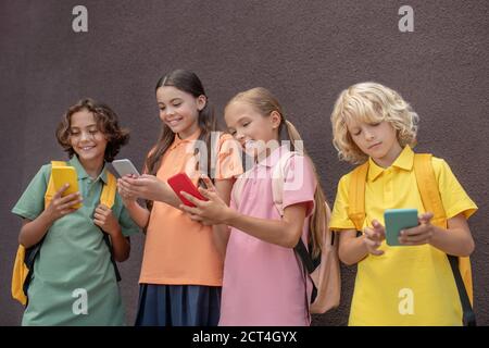 Quattro bambini in piedi l'uno accanto all'altro con smartphone in mani Foto Stock