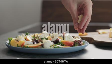 uomo facendo insalata con nettarine e mozzarella su un piatto blu su cemento piano in cucina, aggiungere mandorle fiocchi , foto ampia Foto Stock