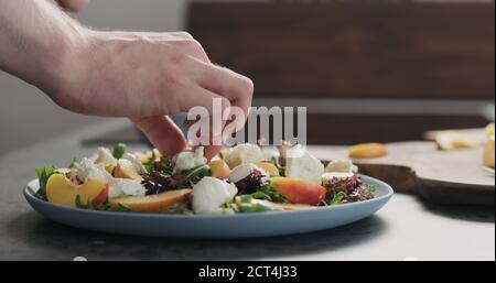 uomo facendo insalata con nettarine e mozzarella su un piatto blu su cemento piano in cucina, aggiungere mozzarella , foto ampia Foto Stock