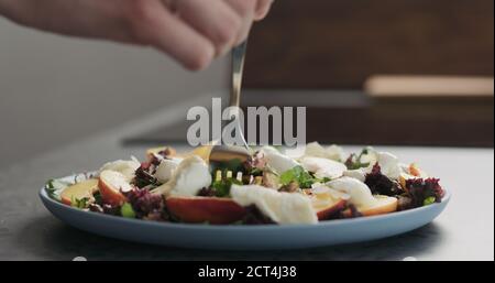 uomo mangia insalata con nettarine e mozzarella su un piatto blu su cemento piano in cucina , foto ampia Foto Stock