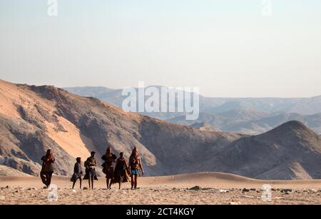 Una famiglia Himba passeggiata attraverso terra sterile nella regione di Kunene, nel nord della Namibia. Foto Stock