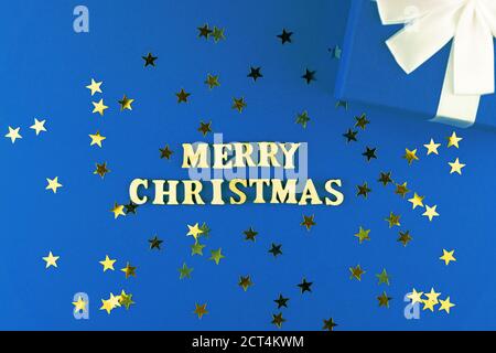 lettere di legno su sfondo blu. Allegra scritta natalizia su carta blu con stelle sparse confetti e confezione regalo Foto Stock