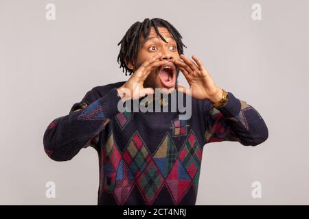 Temuto l'uomo africano preoccupato con i temadlock urlando ad alta voce tenendo le mani vicino a bocca ampiamente aperta, paura, protesta. Studio interno isolato su gr Foto Stock