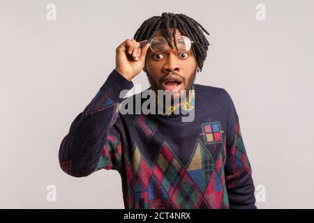 Estremamente scioccato uomo africano domandato con i Dreadlock guardando la macchina fotografica con la bocca ampiamente aperta e gli occhi grandi, mettendo fuori gli occhiali, sorpreso. Interni Foto Stock