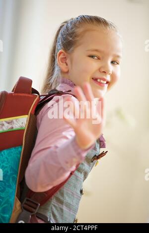 Sorridente ragazza con borsa a mano va a scuola e onde Arrivederci Foto Stock